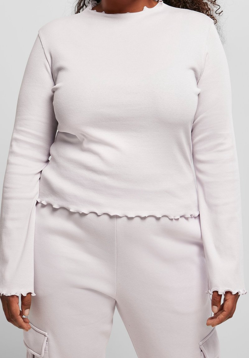 Ljusrosa ribbad långärmad topp med en volang i halsringningen och nederdelen, med åtsittande ärmar och en något kortad design.