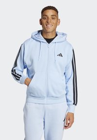 Ljusblå zip-up hoodie med svarta ränder på ärmarna och logotyp. Tillverkad av mjukt material, har en framficka och en justerbar huva.