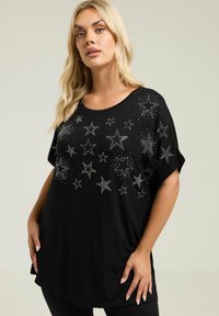 Czarny t-shirt z krótkim rękawem ozdobiony wzorami gwiazd wykonanymi z srebrnych rhinestones. Miękka tkanina o luźnym kroju i zaokrąglonym końcu.