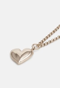 Srebrny wisiorek w kształcie serca na łańcuszku, z polerowanym wykończeniem i grawerowanym logo, z owalnymi ogniwami w designie łańcuszka.