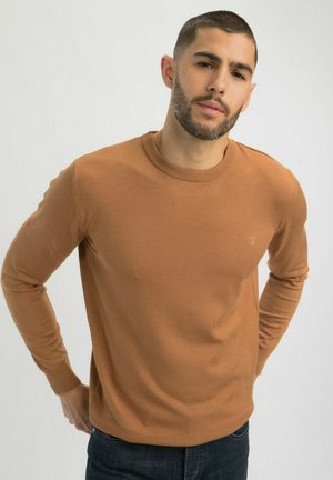 Pull en tricot brun avec un col rond et des manches longues. Présente des poignets et un ourlet côtelés. Design simple avec un petit logo sur la poitrine.