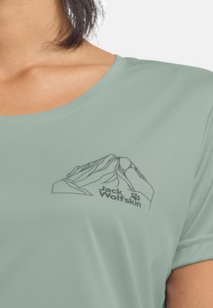 T-shirt sportif vert clair avec un motif de ligne artistique de montagne et le logo "Jack Wolfskin" en noir, col rond et manches courtes.