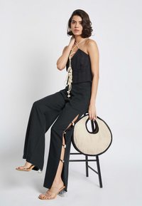 Top corto lavorato a maglia nera con dettaglio allacciato, pantaloni larghi neri con fessure laterali, sandali con tacco trasparente e borsa rotonda in tessuto intrecciato con rifiniture nere.