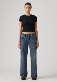 Μαύρο κοντό μπλουζάκι, μπλε τζιν παντελόνι με φαρδιά μπατζάκια, πέντε τσέπες, κούμπωμα με κουμπί και φερμουάρ, και αντίθετο ράψιμο. Φορεμένο με μαύρα παπούτσια.