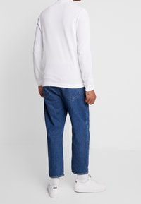 Vit långärmad skjorta i kombination med löst sittande blå denimjeans och vita sneakers, med ribbade cuffs och avslappnad passform.