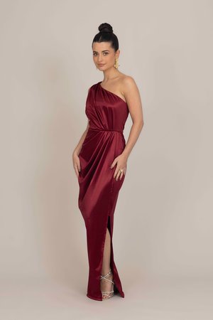 Burgundy satin dress with a one-shoulder design, gathered waist, and a side slit. Smooth texture and a form-fitting silhouette.