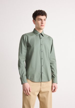 Chemise verte à boutons avec col, manches longues et ourlet arrondi ; fabriquée en tissu lisse, ornée de boutons sombres sur le devant.