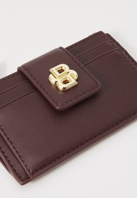 Cardholder din piele maro inchis, cu mai multe sloturi pentru carduri și un clasp cu un dublu logo „B” auriu pe clapeta din față.