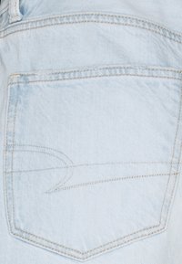 Světle modrá džínová kapsa čtvercového tvaru. Obsahuje kontrastní béžové švy a jemný zakřivený vzor. Měkká textura.