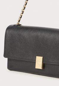 Pochette en cuir noir avec un fermoir géométrique doré et une chaîne. Texture lisse, forme rectangulaire et fermeture à rabat.