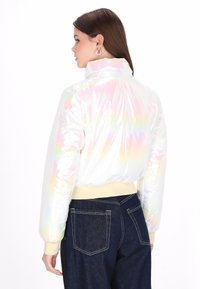 Irideszkáló, rövidített pufajka magas nyakkal, sima, fényes textúrával, valamint kontrasztos bordás mandzsettákkal és aljjal.