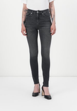 Jeans skinny taille haute en denim gris foncé, dotés d'un design classique à cinq poches et d'un léger délavage, associés à des chaussures à talons hauts noires.