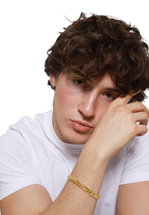 Goldene Kettenarmband an einem Handgelenk, mit verflochtenen Gliedern. Das Modell trägt ein schlichtes weißes T-Shirt und hat lockiges braunes Haar.