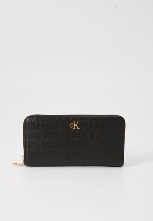 Czarny portfel w tłoczenie w wzór krokodylej skóry, z złotym logo 'cK'. Zamek błyskawiczny i gładka powierzchnia. Prostokątny kształt z eleganckim designem.