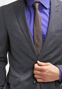 Grijze jas met een slim fit, voorzien van een soepele textuur, notch-kleppen en twee knopen. Draagt een paarse blouse en een bruine stippelstrik.