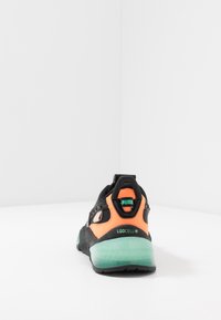 Sneaker Puma LQDCell nera e arancione vista dal retro, con suola verde traslucida e tab con logo sul tallone.
