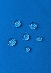 Tessuto blu con una superficie textured, caratterizzato da diverse gocce d'acqua rotonde che riflettono la luce, disposte in modo casuale sulla material.