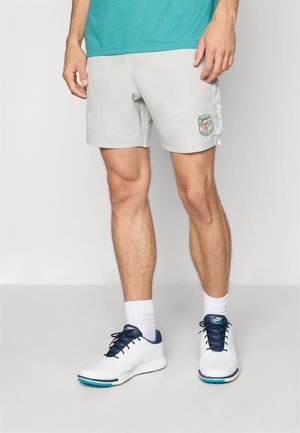 Lyse grå badetøyshorts med et brodert logopatch, sidelommer og snøring i livet. Kombinert med hvite sneakers og hvite sokker.