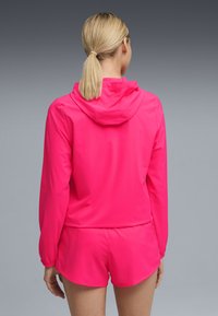 Ροζ ελαφρύ μπουφάν με κουκούλα και μακριά μανίκια, συνδυασμένο με αντίστοιχα σορτς. Λείο υλικό, αθλητικός σχεδιασμός, με ελαστικές μανσέτες.