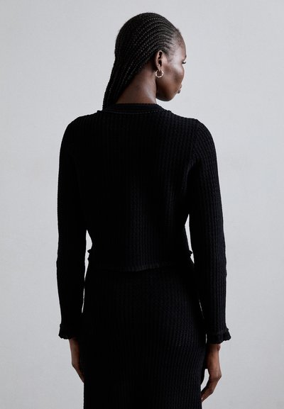 Musta ribbed neule cropped pusero pitkilla hihalla ja repsottavilla reunoilla, jossa on teksturoitu muotoilu ja pyöreä kaula-aukko.