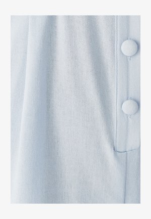 Svetlo modra tkanina ima teksturirano tkane površje z vrsto treh okroglih gumbov na desni strani, kar dodatno obogati oblikovanje.