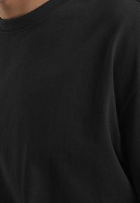 Černé crewneck tričko vyrobené z měkké bavlny, s vroubkovaným výstřihem a hladkou texturou, bez viditelných vzorů nebo akcentů.