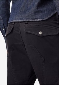 Černé, lehké kalhoty s úhlovými kapsami a viditelným šitím. Pas má kovové zapínání na knoflík a látka má hladký povrch.