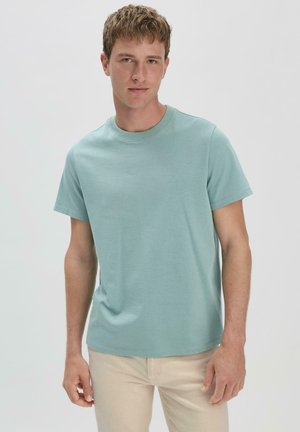 T-shirt bleu clair à col rond en tissu doux, avec des manches courtes et une coupe décontractée, associée à un pantalon beige clair.