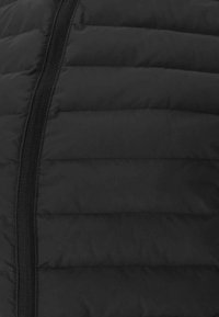 Schwarze gepolsterte Weste mit gesteppten Abschnitten und einem zentralen Reißverschluss. Glatte Textur mit einem eleganten, schlanken Design.