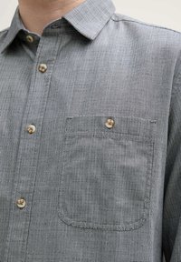 Chemise à boutons avec un motif rayé noir et blanc, dotée d'une poche poitrine, d'un col pointu et de boutons beiges. Finition en tissu texturé.