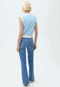 Top de punto sin mangas de color azul claro con cuello de canalé blanco, combinado con jeans azules de talle alto y acampanados. Textura suave, diseño casual.