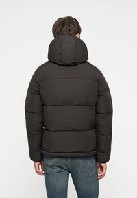 Puffjakke i solid sort, med høj krave og quiltede sektioner for isolering, parret med blå jeans.