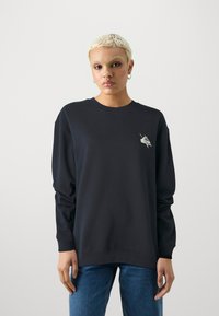 Marinblå sweatshirt med långa ärmar, rundad halsringning och ribbade muddarna. Har en liten vit grafisk design på vänster bröst.