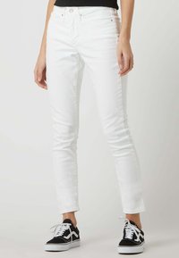 Pantalones vaqueros blancos ajustados de denim, con una cintura alta, textura suave y sutiles detalles de costura, combinados con zapatillas negras.
