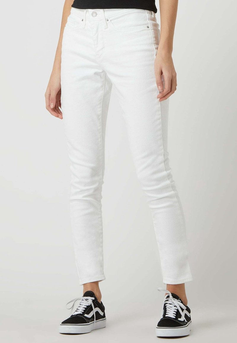 Pantalones vaqueros blancos ajustados de denim, con una cintura alta, textura suave y sutiles detalles de costura, combinados con zapatillas negras.