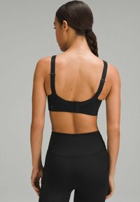 Sujetador deportivo negro con tirantes ajustables, panel trasero texturizado y cierre de gancho. Llevado con unos leggings negros de cintura alta a juego.