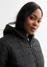 Chaqueta de plumas negra con diseño acolchado, que cuenta con una capucha y cierre delantero. El material es suave y brillante. Los acentos incluyen un cierre con un patrón.