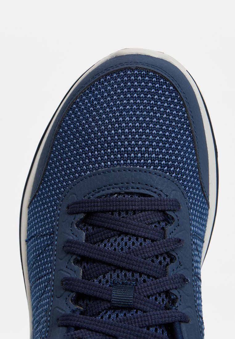 Zapatilla deportiva azul marino con parte superior de malla texturizada, cierre de cordones, puntera reforzada y suela de goma de color claro.