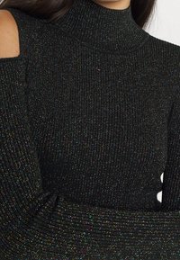 Czarny prążkowany golf z błyszczącymi metalicznymi nitkami, z odkrytymi ramionami i długimi rękawami.