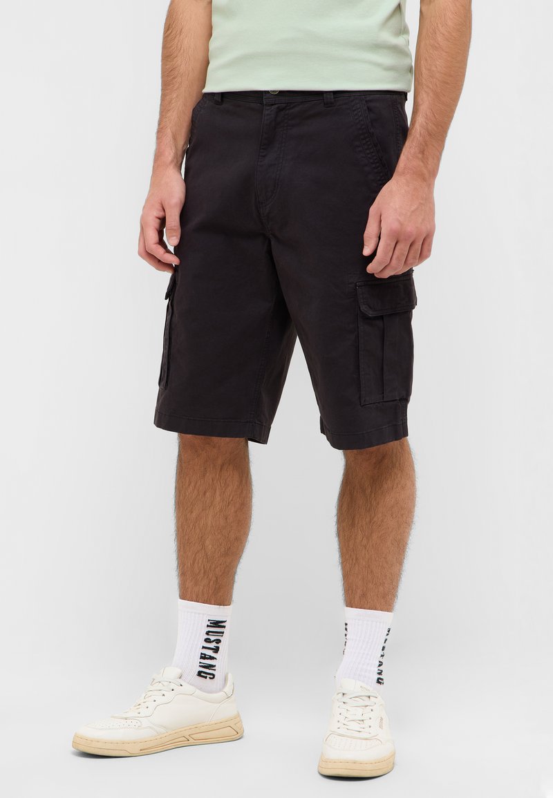 Czarne szorty cargo wykonane z bawełny, z dwiema bocznymi kieszeniami, luźnym krojem i nogawkami sięgającymi powyżej kolana. Noszone z białymi trampkami.