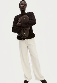 Sort kabelstrikket sweater med frynset kant, cremefarvede vidde bukser og en brun taske med gulddetaljer. Ensfarvede, afslappet pasform.