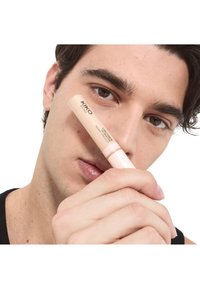 Homme tenant le correcteur lumineux KIKO Milano Love Fusion près du visage, mettant l'accent sur les yeux et le texte du produit.