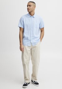 Camisa de manga corta celeste con diseño de botones y bolsillo en el pecho, combinada con pantalones cremosos y zapatillas negras. Un look simple y limpio.