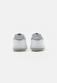 Baskets blanches en cuir et maille avec un contrefort de talon gris. Présente un marquage New Balance à l'arrière et une semelle en gomme texturée.