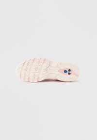 Egy rózsaszín és fehér New Balance sportcipő talpa, texturált tapadással és kék ovális betétekkel a sarok területén.