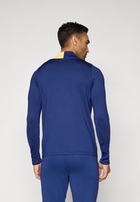 Marineblå langermet treningstopp med detalj i gul krage, laget av glatt stoff, med slim fit og minimale sømmer.