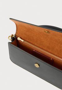 Črna usnjena torba z notranjostjo iz rjavega žameta, ki vsebuje žep z zadrgo in okras z zlato-toniranim logotipom.