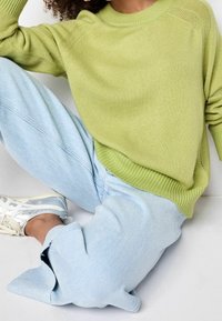 Pull en laine verte avec un col à côtes, associé à un pantalon de jogging bleu clair. Baskets argentées et blanches avec des accents réfléchissants.