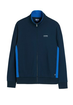 Granatowa kurtka na zamek z jasnoniebieskimi bocznymi panelami, prążkowanymi mankietami i dołem oraz logo "Diverse Nautical Club" na piersi.