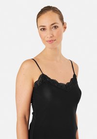 Camisola nera con un bordo in pizzo lungo lo scollo. Presenta spalline sottili e regolabili e una texture liscia. Design aderente.